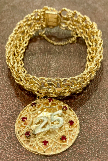 a gold chain bracelet with a large golden pendant with the number 25 and accented with red gems