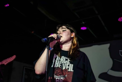Person in a black Pierce the Veil shirt grabs a microphone and sings into it.