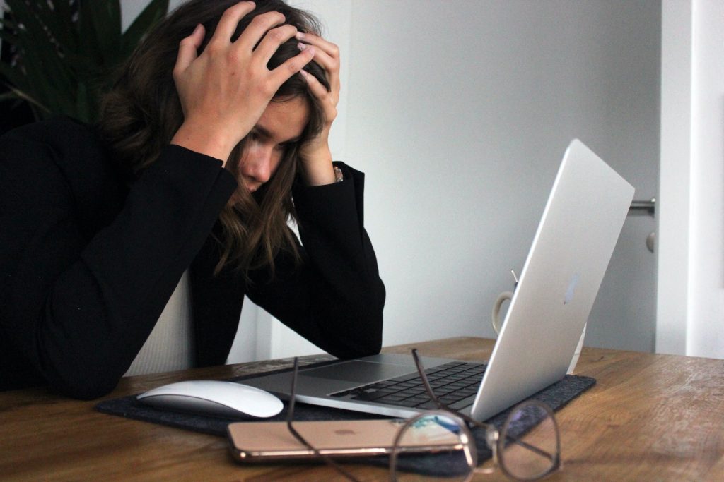 Person holding their head in their hands in front of a computer