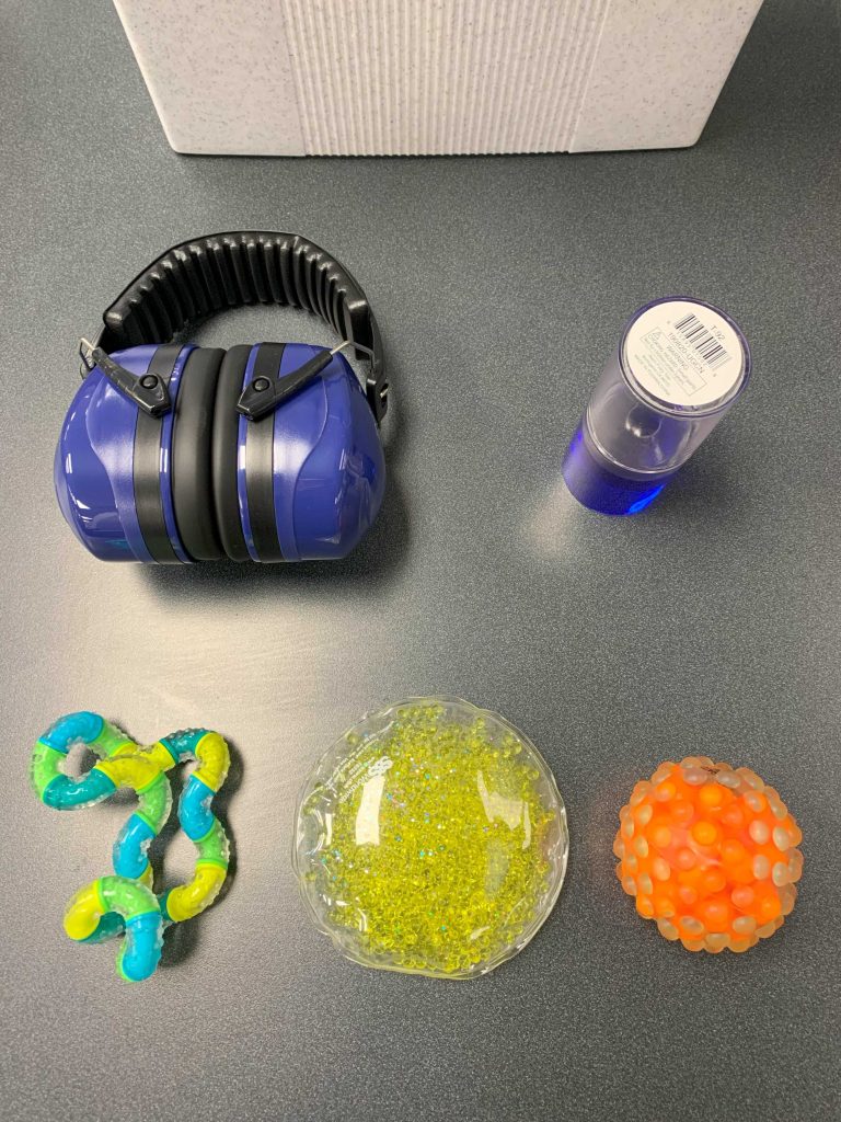 Three hand-sized stress toys, a pair of large headphones, and a clear tube with blue ooze.