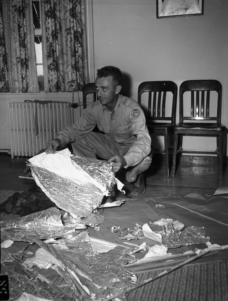 Maj. Jesse A. Marcel of Houma, La (looking left) and holding pieces of foil lined material related to Roswell, New Mexico.