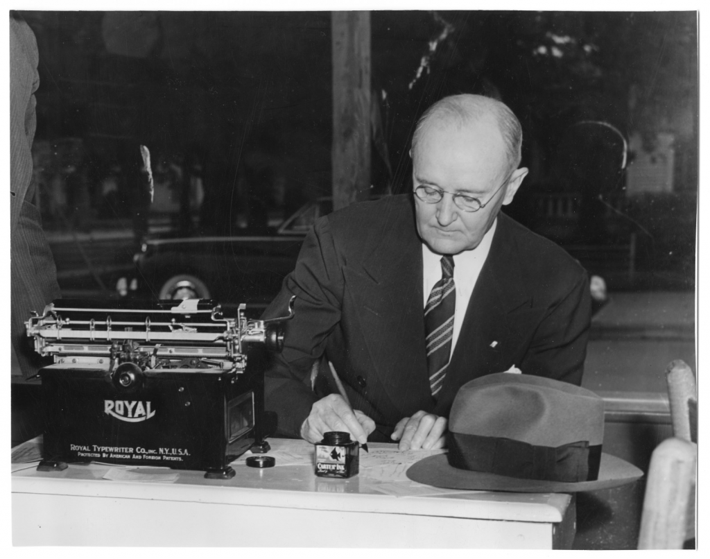 Photo of North Texas State Teachers College President W.J. McConnell at his desk, signing a document.