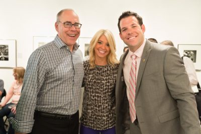 Neal Smatresk, Amanda Quinn, and Johnny Quinn posing together. People and the wall of an art gallery are visible behind them.
