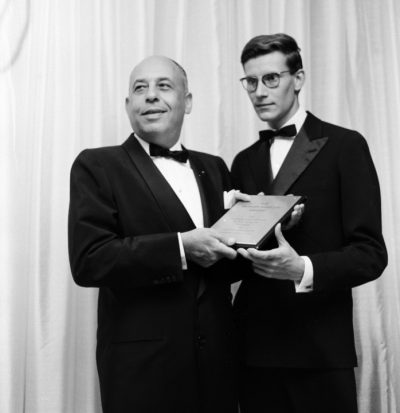 Black and white photograph of Stanley Marcus and Yves St. Laurent posing for a photo holding an award.